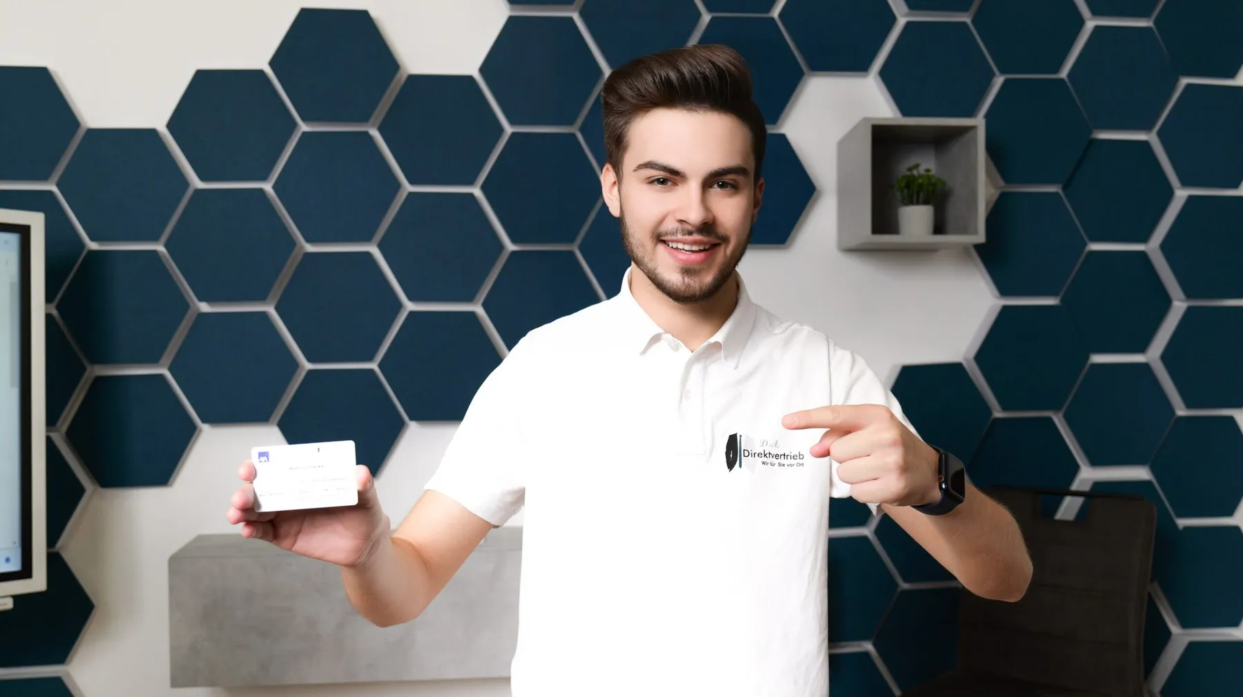 Mitarbeiter von D.A. Direktvertrieb präsentiert vor der Firmen-Hexagonwand ein Produkt